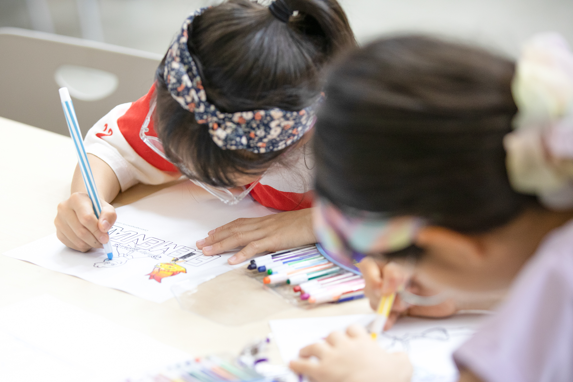 책상에서 두 어린이가 집중해서 색연필로 그림을 색칠하고 있는 사진